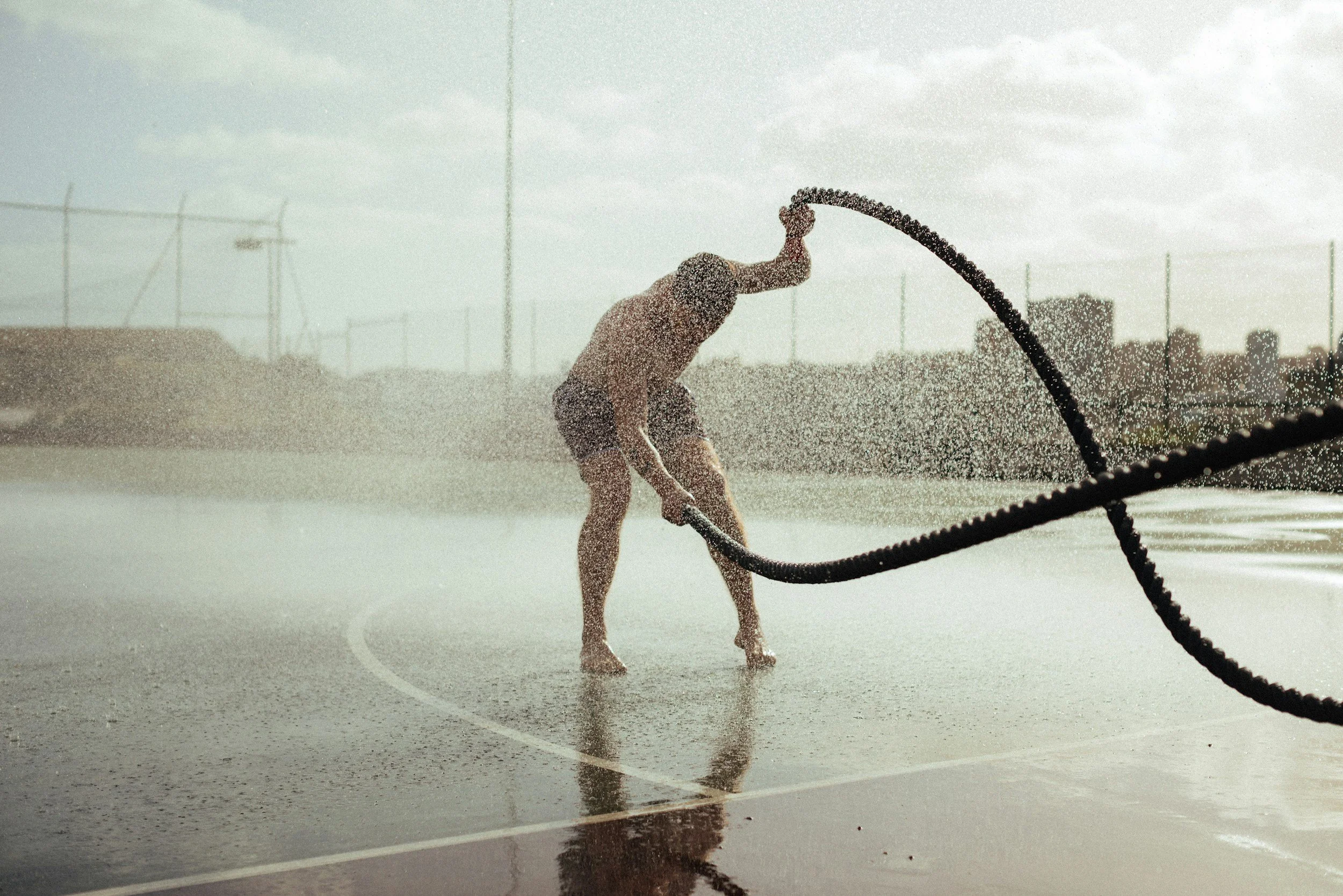 A person playing tennis on an outdoor court, holding a tennis racket with water spraying around them, likely after getting wet or during rain.