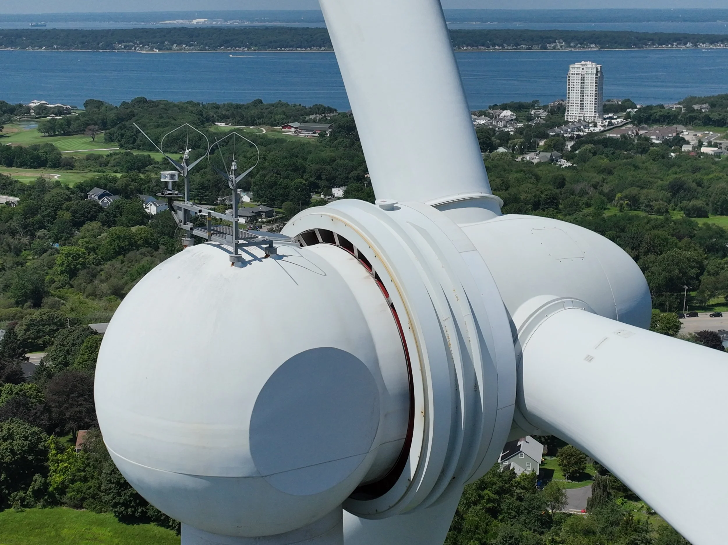 Close aerial view of a wind turbine nacelle and blade hub above Portsmouth, Rhode Island.