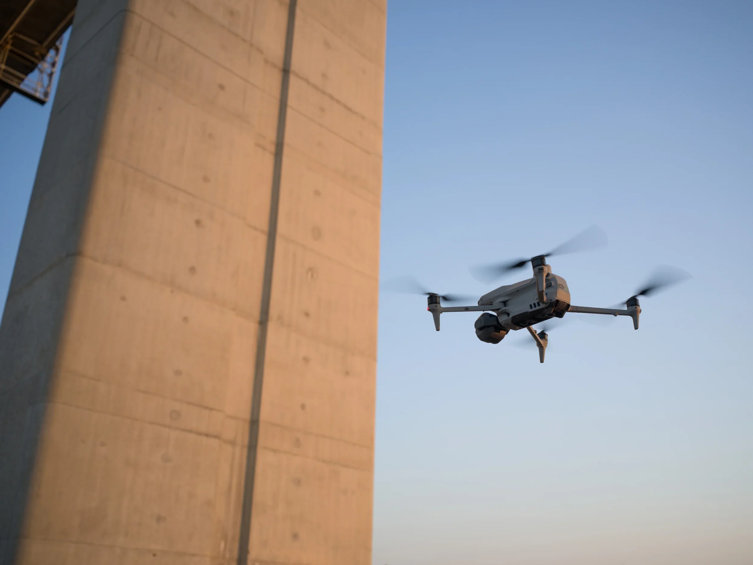 A drone flying in the sky near a concrete bridge during daytime.