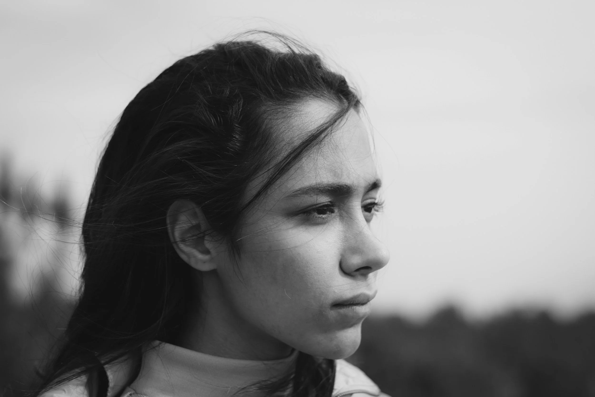 Black and white close-up of a woman's face in profile, with her eyes slightly closed and her hair blowing in the wind.