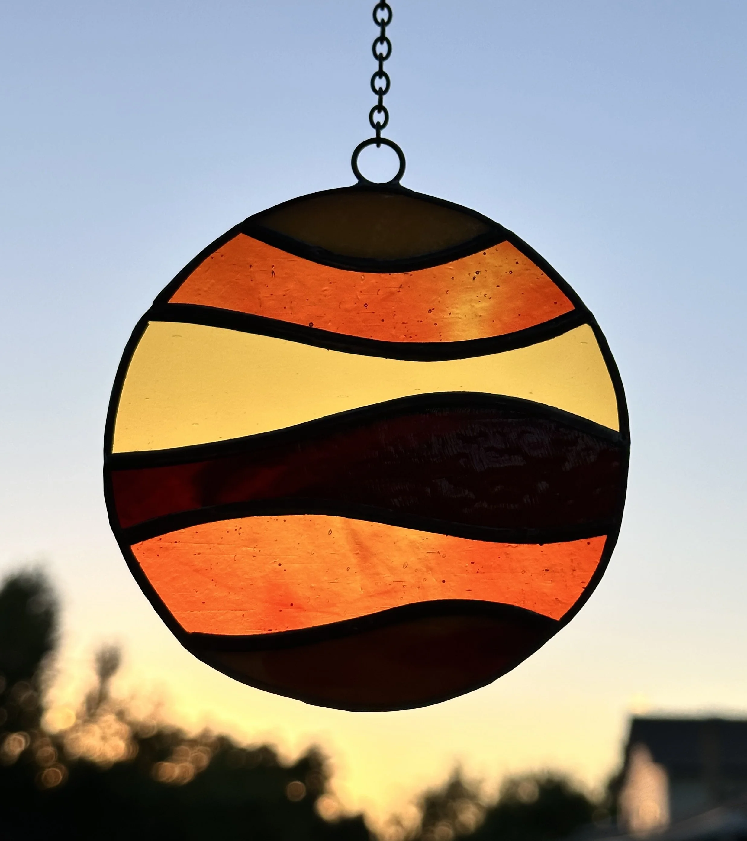 Close-up of a stained glass suncatcher hanging outdoors against a sunset sky.