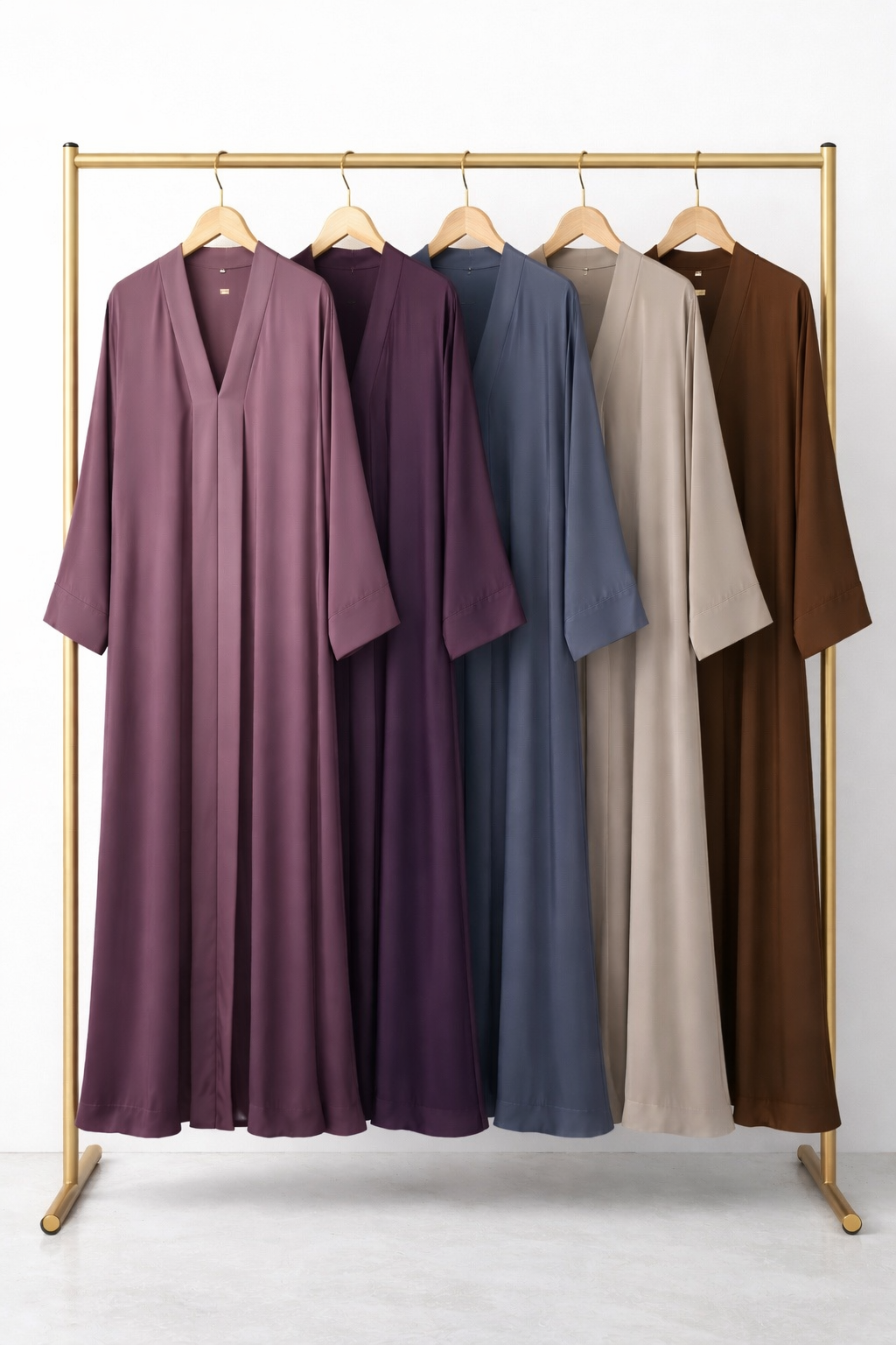 Five long, satin robes in shades of pink, purple, blue, beige, and brown hanging on a gold clothing rack.