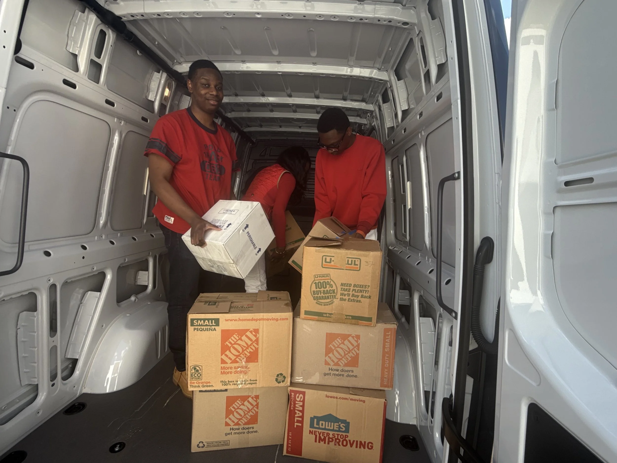 Three people packing boxes in the back of a moving van. The boxes are labeled from The Home Depot and Lowes, and there are a variety of sizes.