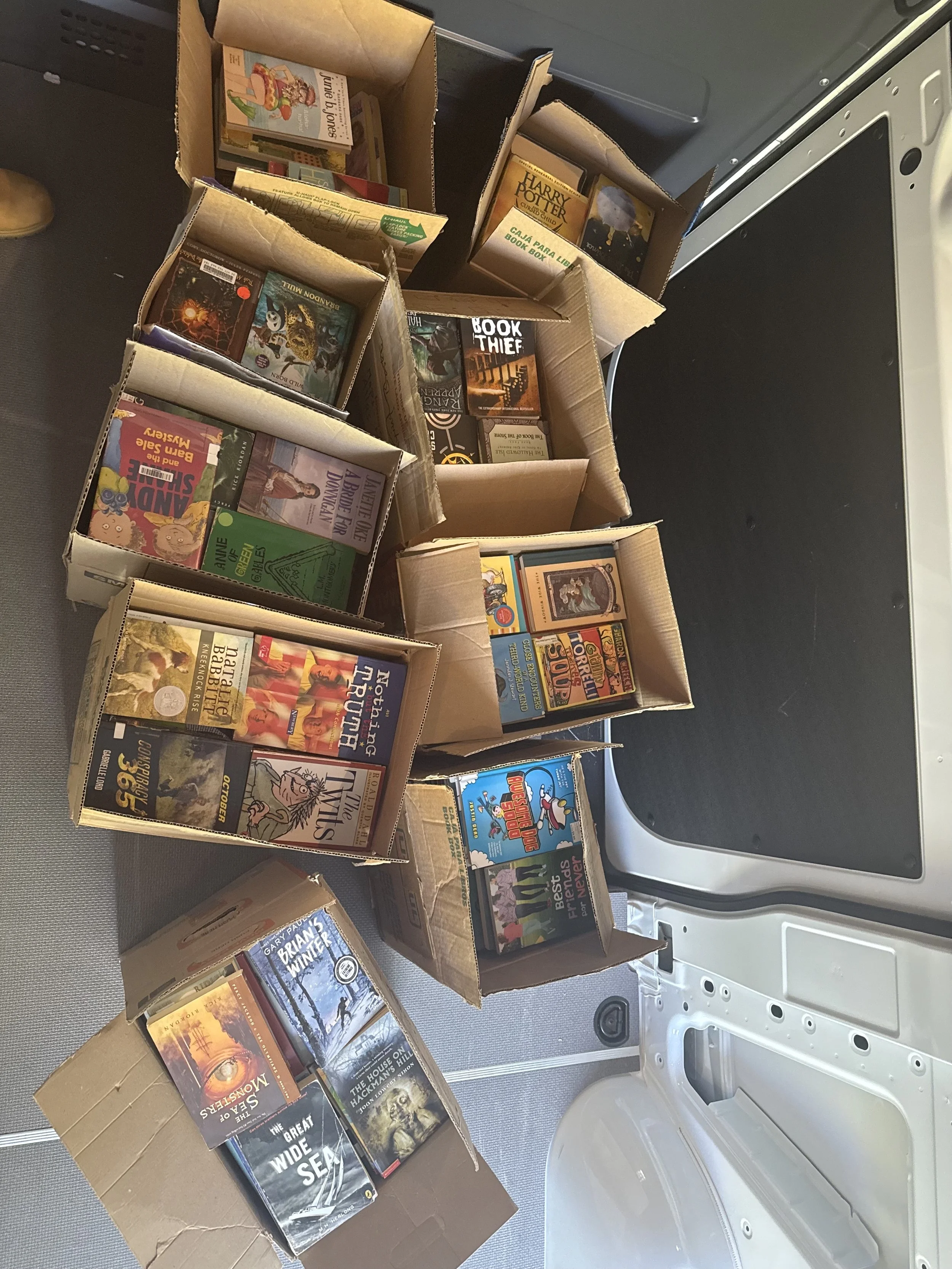 Several cardboard boxes filled with books on a gray surface next to an open white and black appliance, possibly a dryer or washing machine.