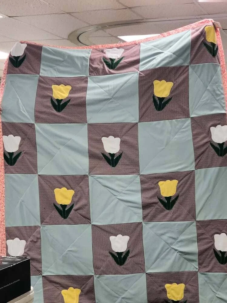 A quilt with a checkered pattern featuring white and yellow tulip appliqués.