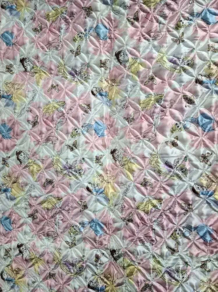 Patterned fabric featuring illustrations of young girls with pigtails in yellow, purple, and blue dresses, surrounded by butterflies on a quilted pink and white background.
