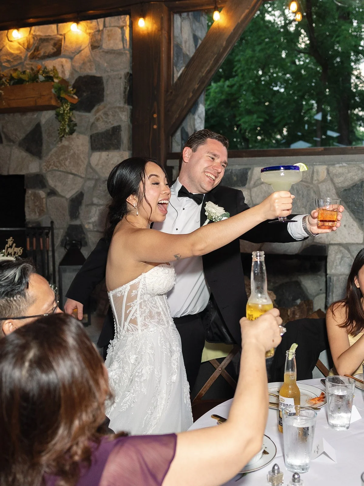 A bride and groom at their wedding reception celebrating with friends, holding drinks and smiling.