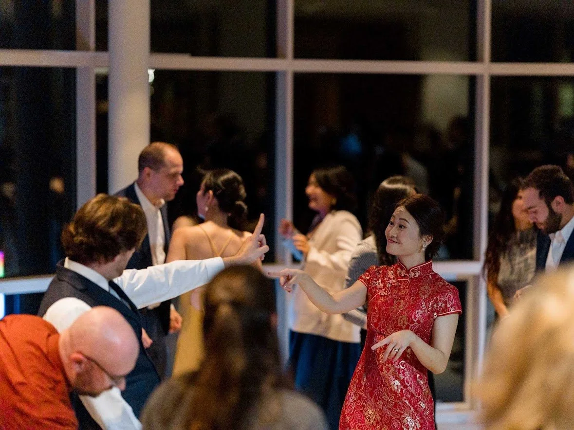 People dancing and socializing at an indoor event, with a woman in a red dress pointing and smiling.