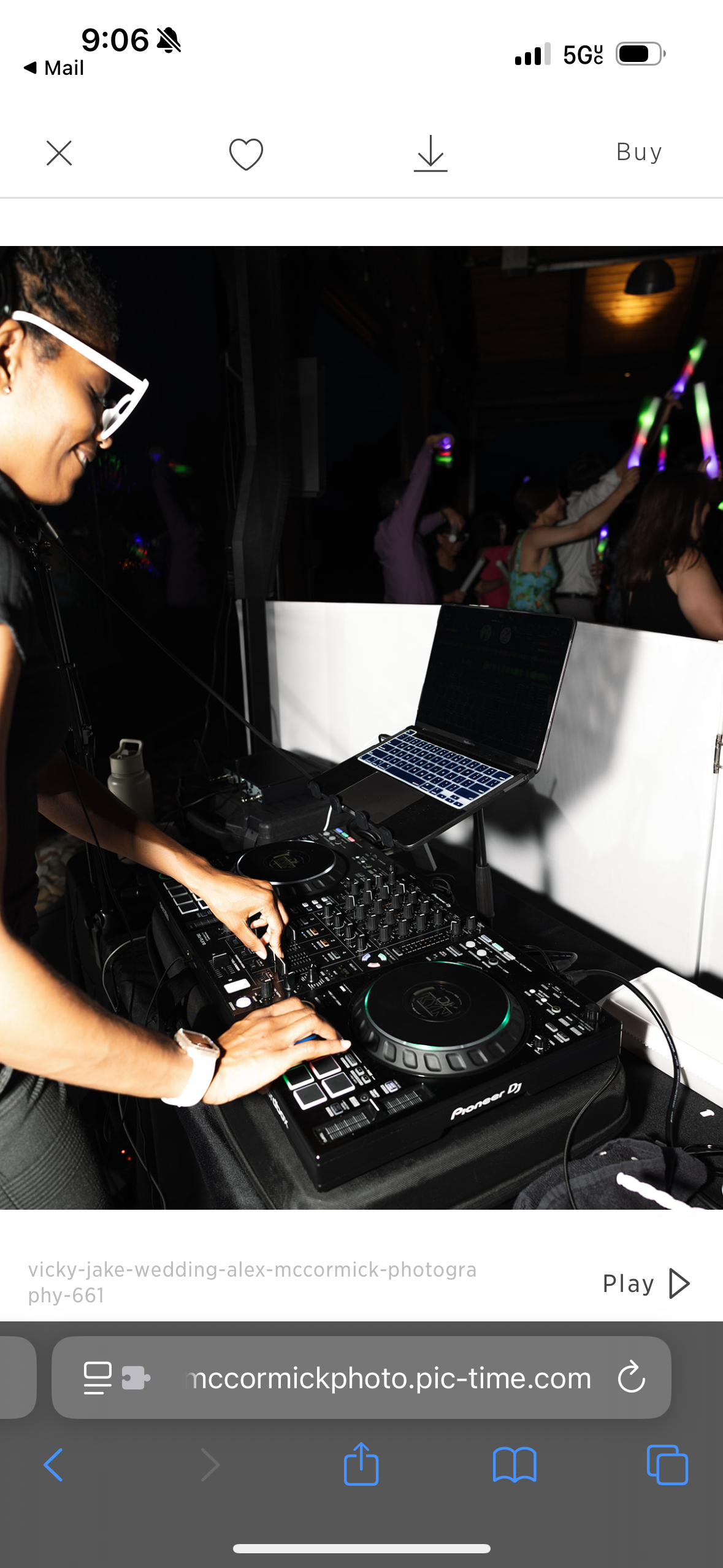 A DJ performing at a nightclub, using a mixing console, with a laptop on a stand, and people dancing in the background under colorful lights.