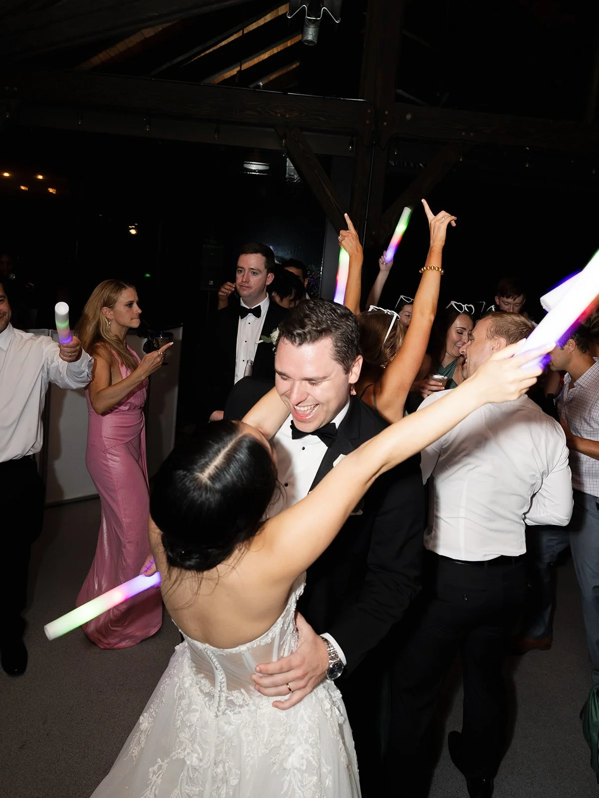 Couple dancing at wedding reception with partygoers around them, holding glow sticks, celebrating and enjoying the night.