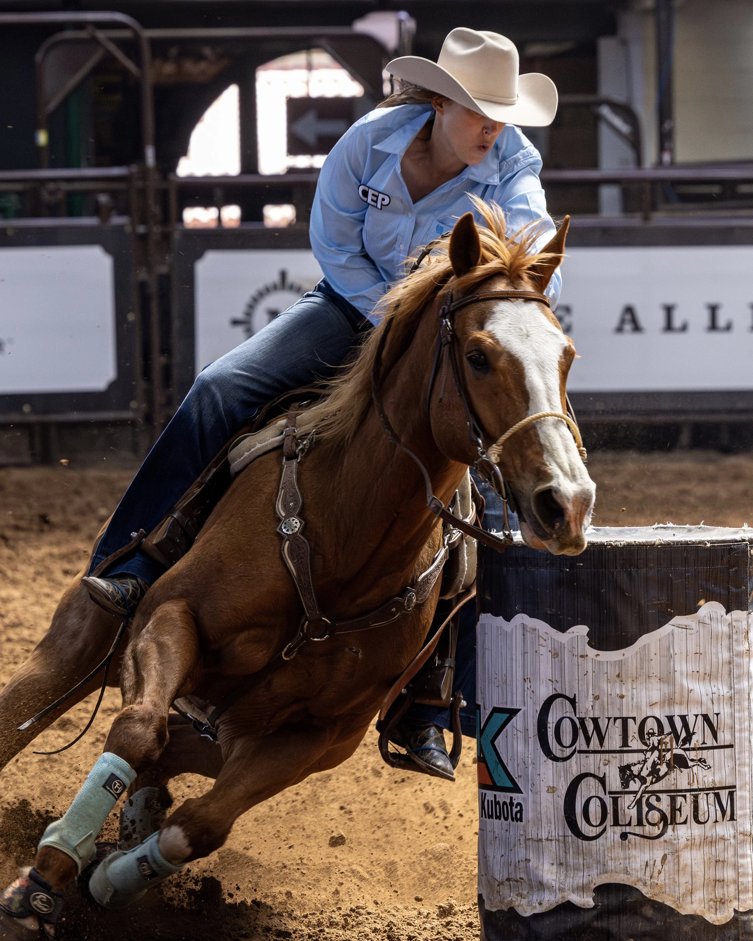A woman in cowboy attire riding a brown and white horse during a rodeo event, with a banner that reads 'Cowtown Giese Museum' behind her.