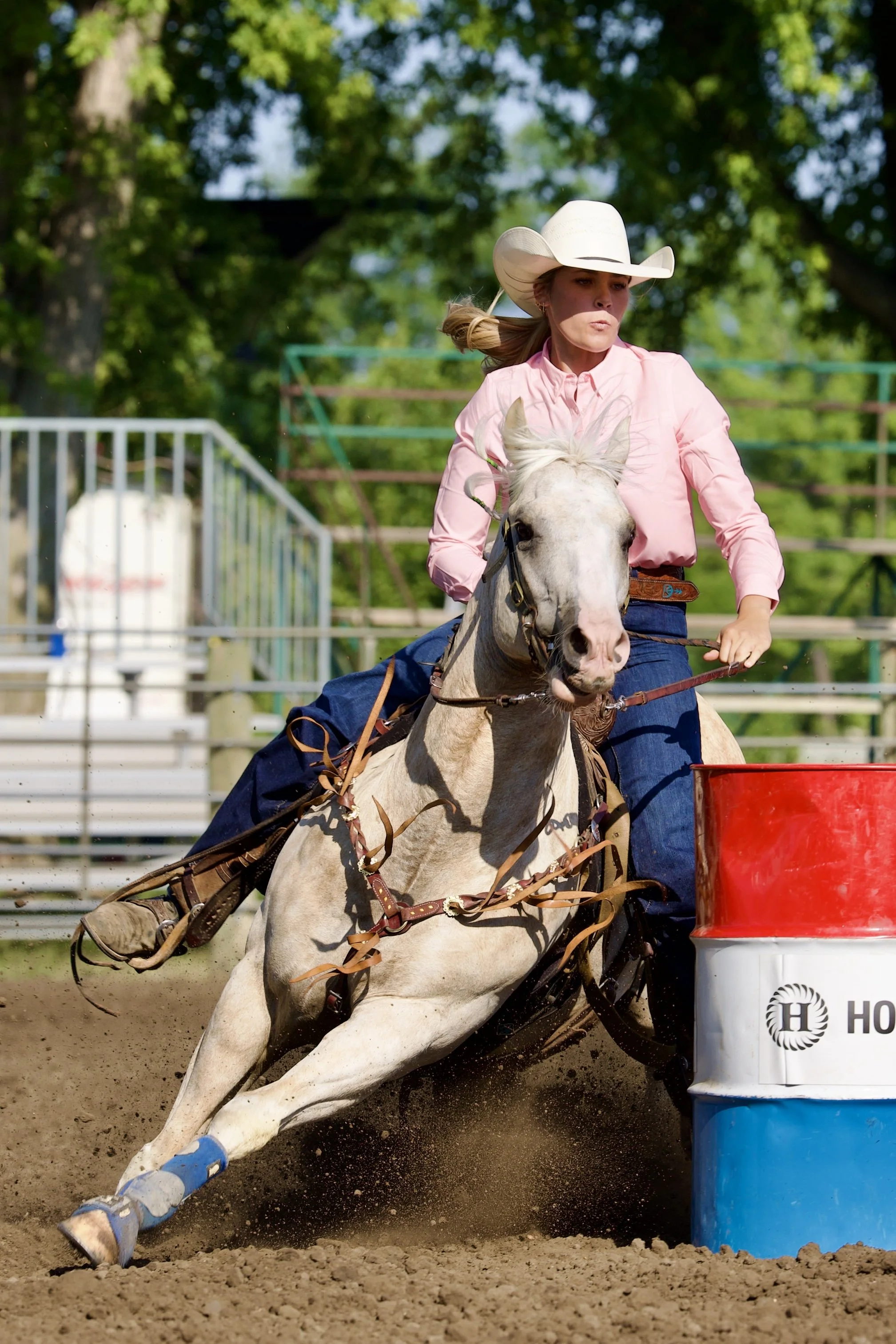 A female rodeo competitor riding a bucking horse around a barrel during a barrel racing event.