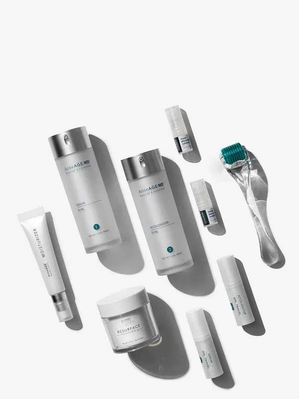 Skincare products and tools on a white surface, including bottles labeled 'AnteAGE MD', a jar labeled 'Resurface', a small tube labeled 'Moisturizer', a roller massager, and small containers.