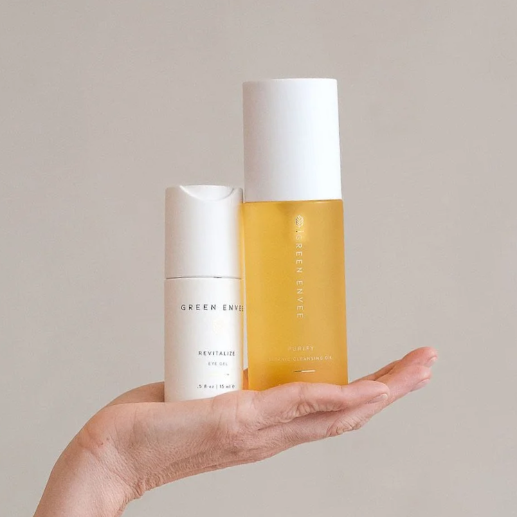 Hand holding two skincare bottles, one white and one yellow, on a plain background.