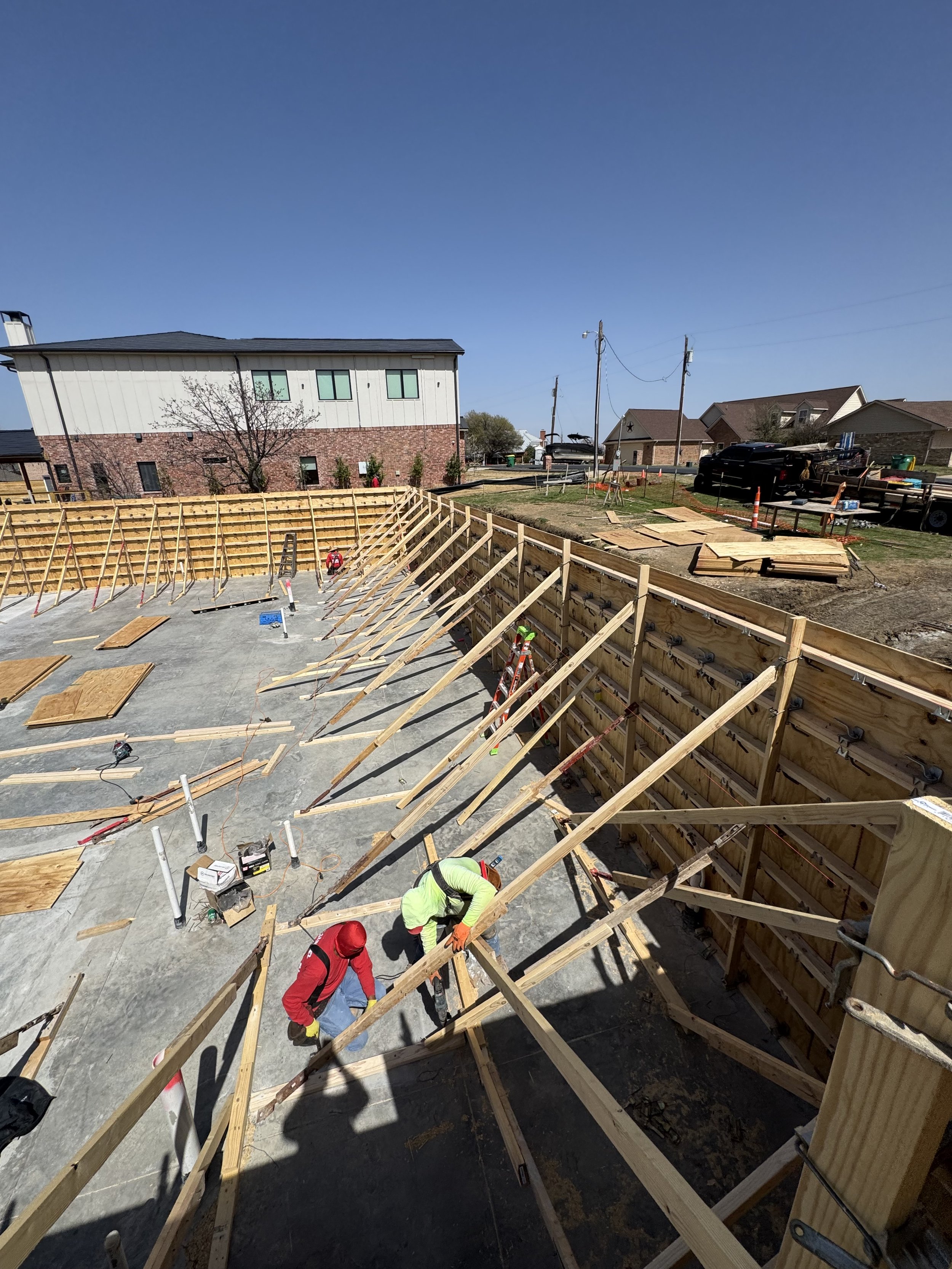 Construction workers building a wooden framework for a new structure in a residential neighborhood on a sunny day.