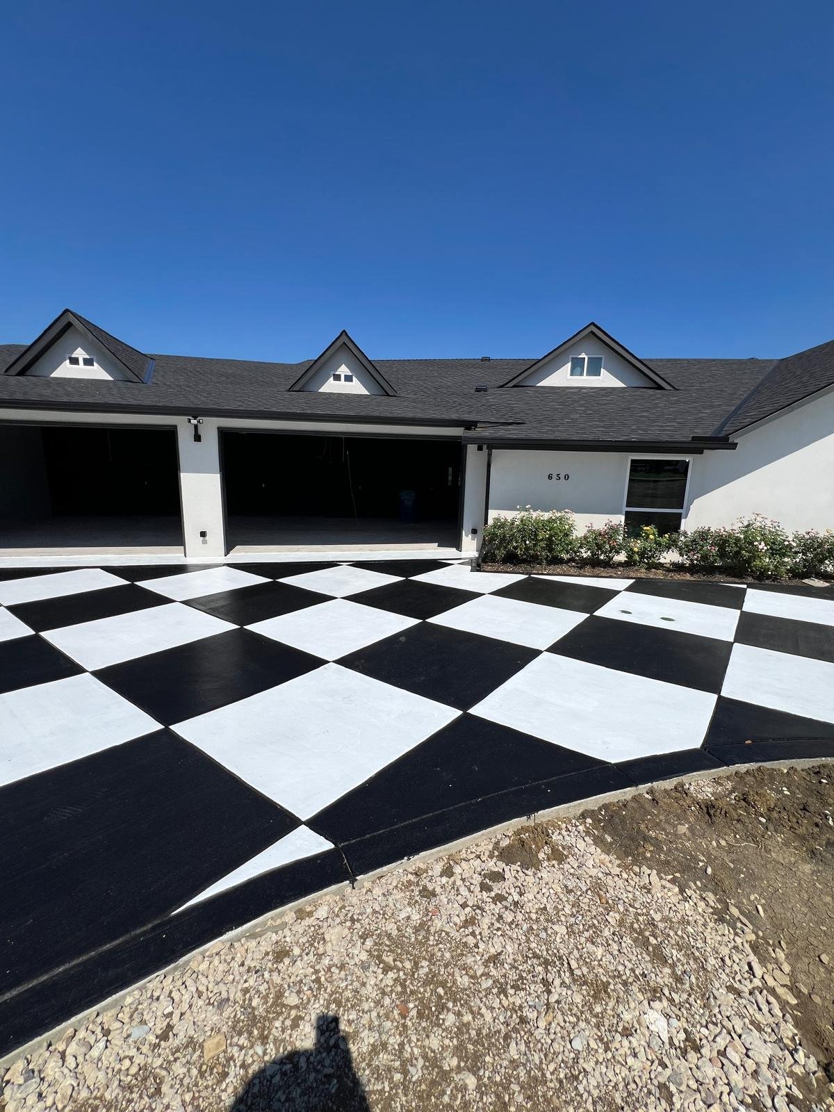 Newly paved black and white checkered driveway in front of a modern white house with a garage and small garden.