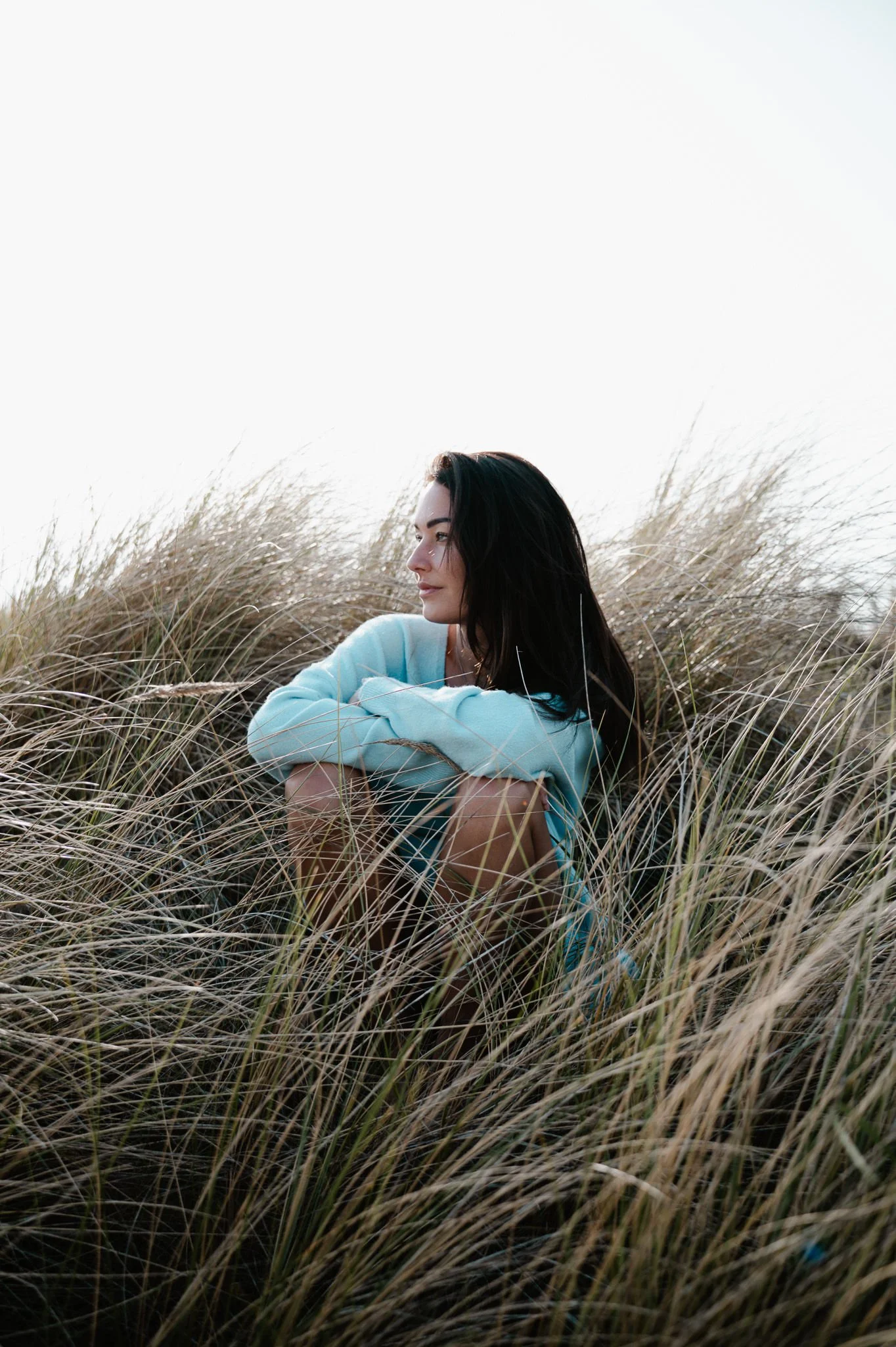 Vrouw zittend in de duinen die rust en innerlijke helderheid ervaart na het doorbreken van patronen