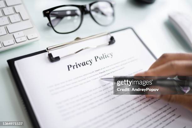 A person is reviewing a privacy policy document on a clipboard with written text, accompanied by a pair of glasses and a pen on a desk.