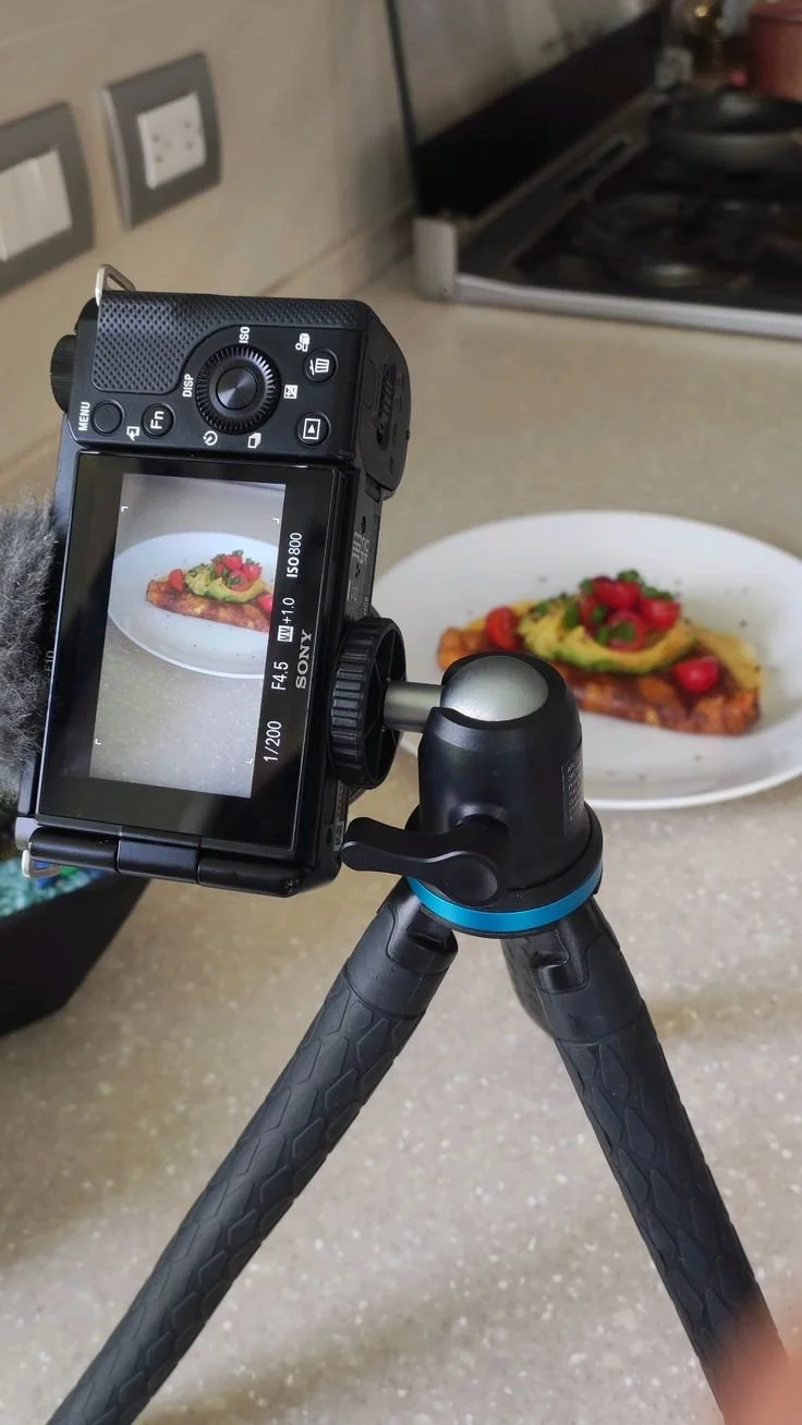 Appareil photo numérique sur un trépied photographiant une assiette de nourriture avec avocat, tomates cerises et filet de poisson