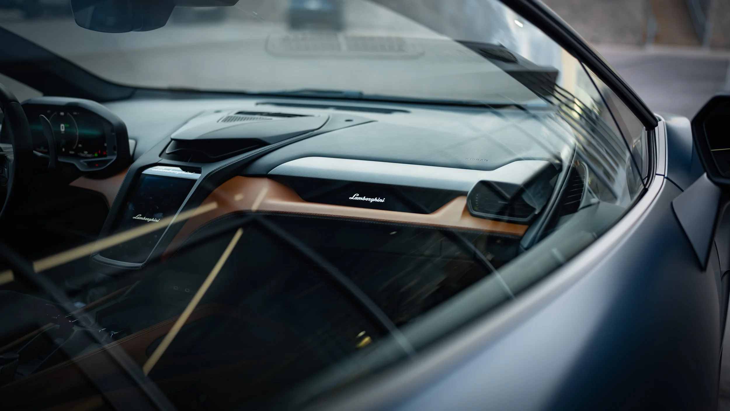 Interior of a Lamborghini luxury sports car, showing the dashboard and steering wheel as seen from outside through the windshield.