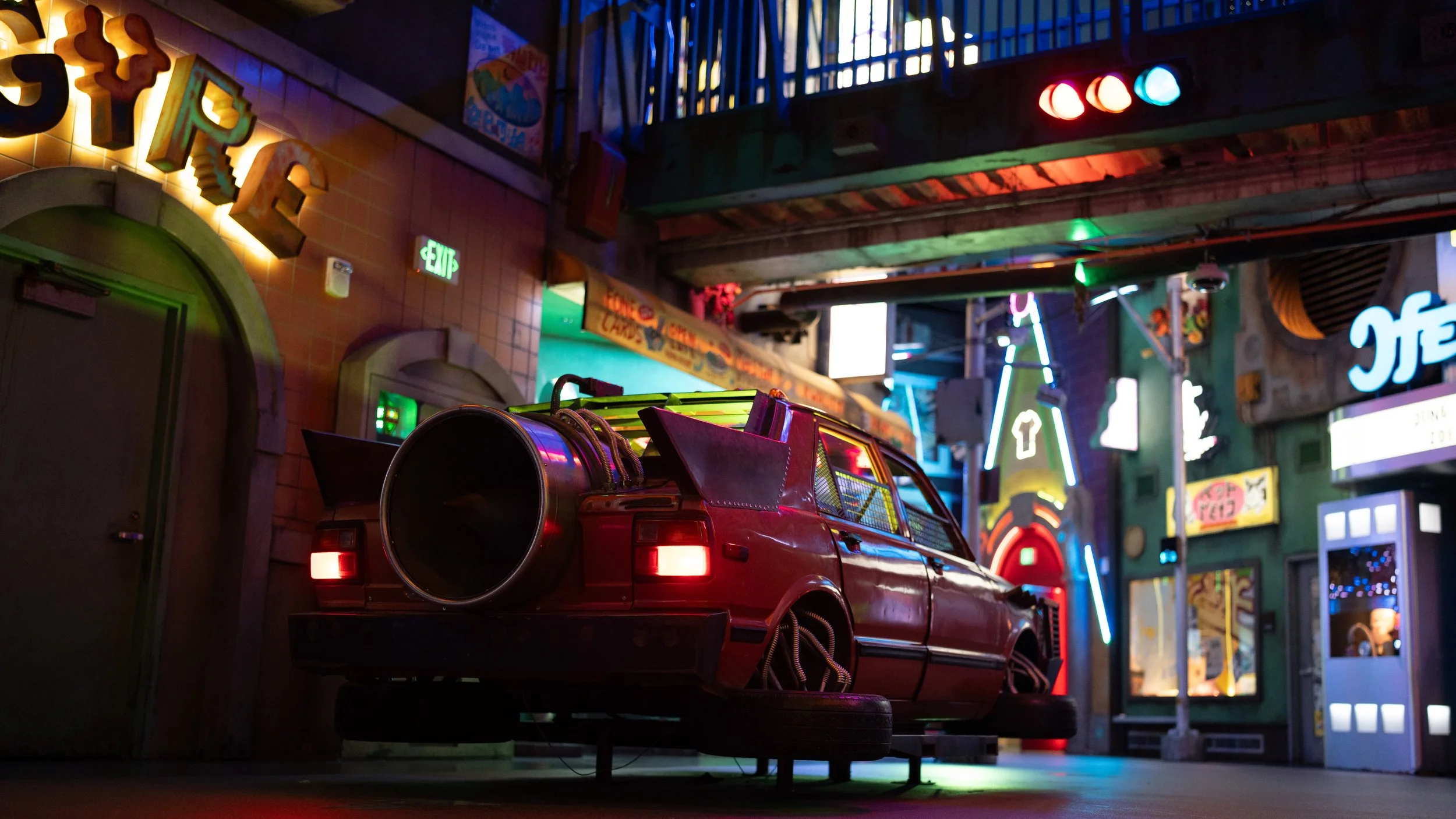 Cluttered indoor space with neon signs, colorful lights, and a red pickup truck with a large speaker on its bed.