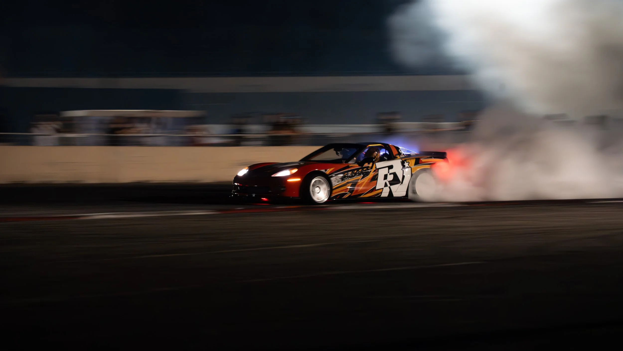 A race car with colorful graphics and the number 73 on its side drifting at night, producing smoke from the tires.