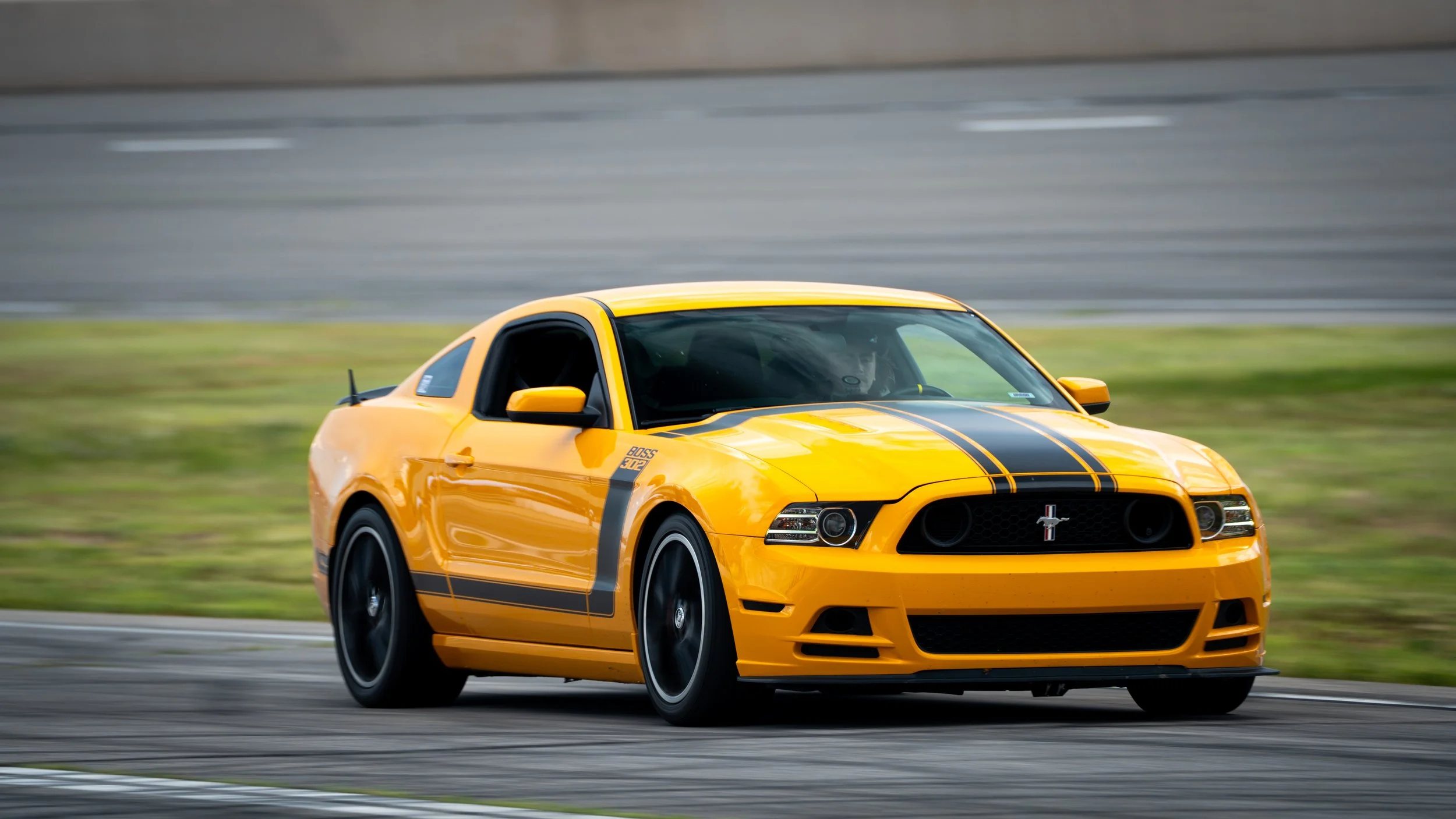 A yellow Ford Mustang sports car with racing stripes on a racetrack.