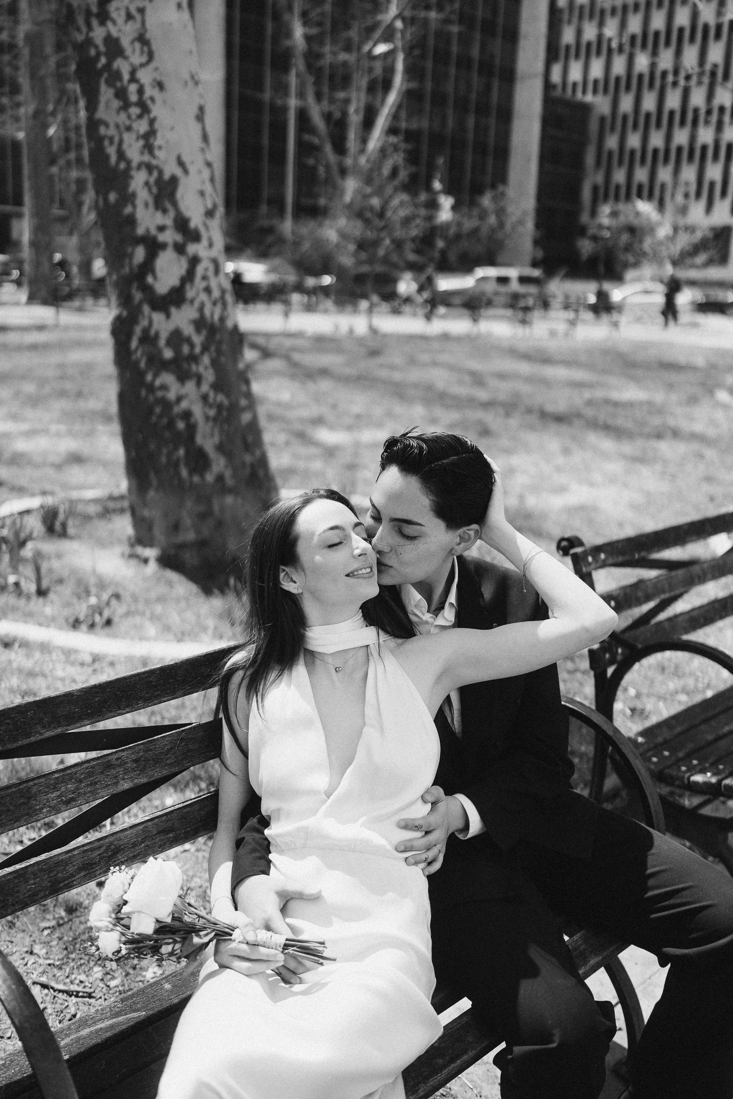 A newlywed couple sharing a romantic kiss on a park bench during their New York City courthouse wedding photo shoot.
