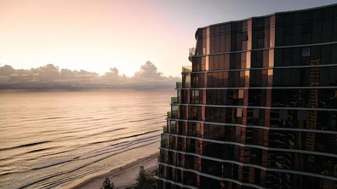 Sunset over the ocean with a modern dark-colored high-rise building on the right side.