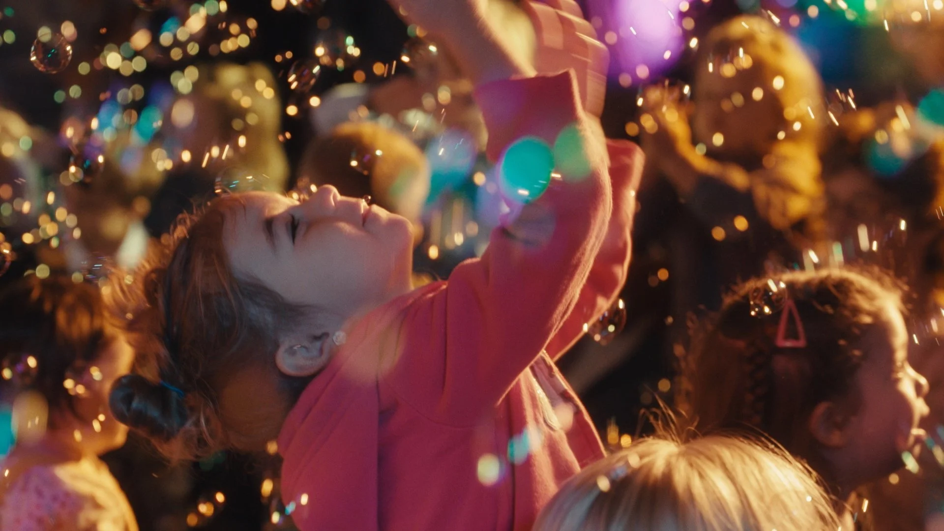 A young girl with red hair and earrings looking up at colorful Christmas lights and ornaments with a joyful expression. Happy And You Know It documentary.