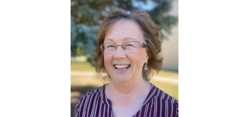 Smiling woman with glasses and earrings outdoors, wearing a striped shirt.