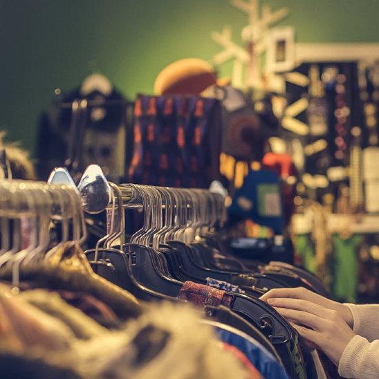 a person's hands showing as they look through a rack of clothes in a thrift store