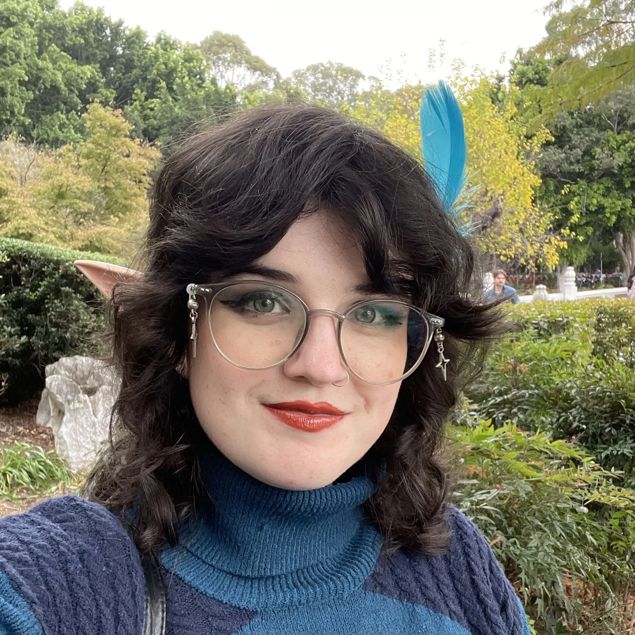 Selfie of a person with glasses and a red lip in a garden.