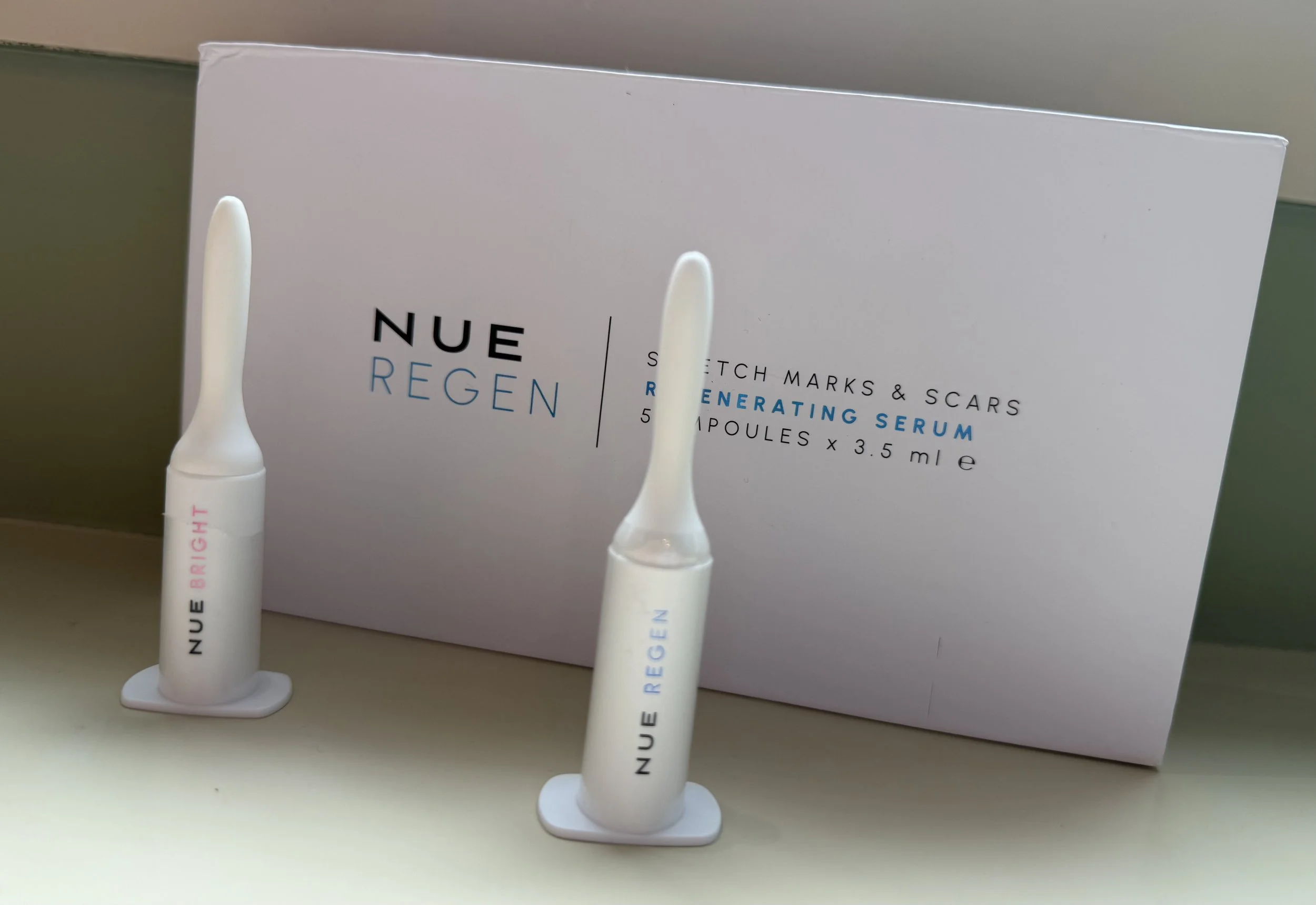 Two white vials with dropper applicators labeled 'NUEREGEN,' positioned in front of a white box with text describing the product, including ingredients and usage instructions.