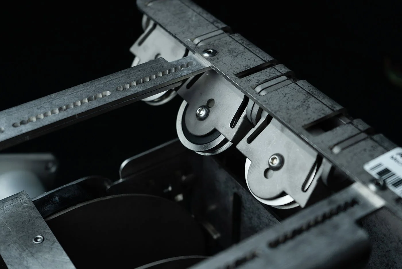 Close-up of a metal mechanical component with rollers and screws, likely part of a machine or conveyor system.