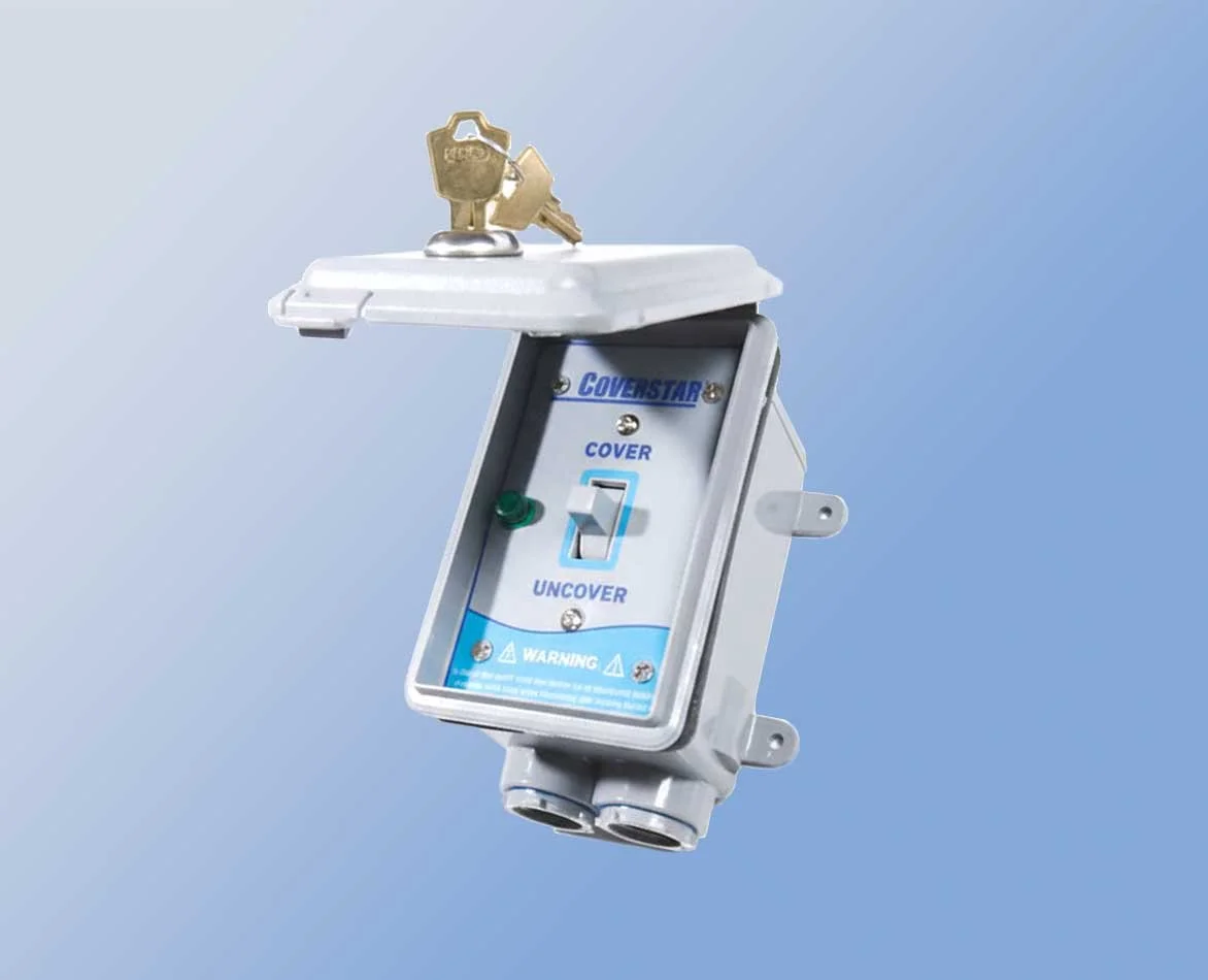 Electrical switch box with a green button and a switch labeled 'Cover' and 'Uncover,' with keys placed on top of it, against a gradient blue background.