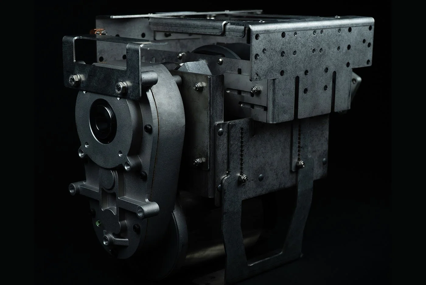 A metallic engine component with various gears and structural parts, photographed against a black background.