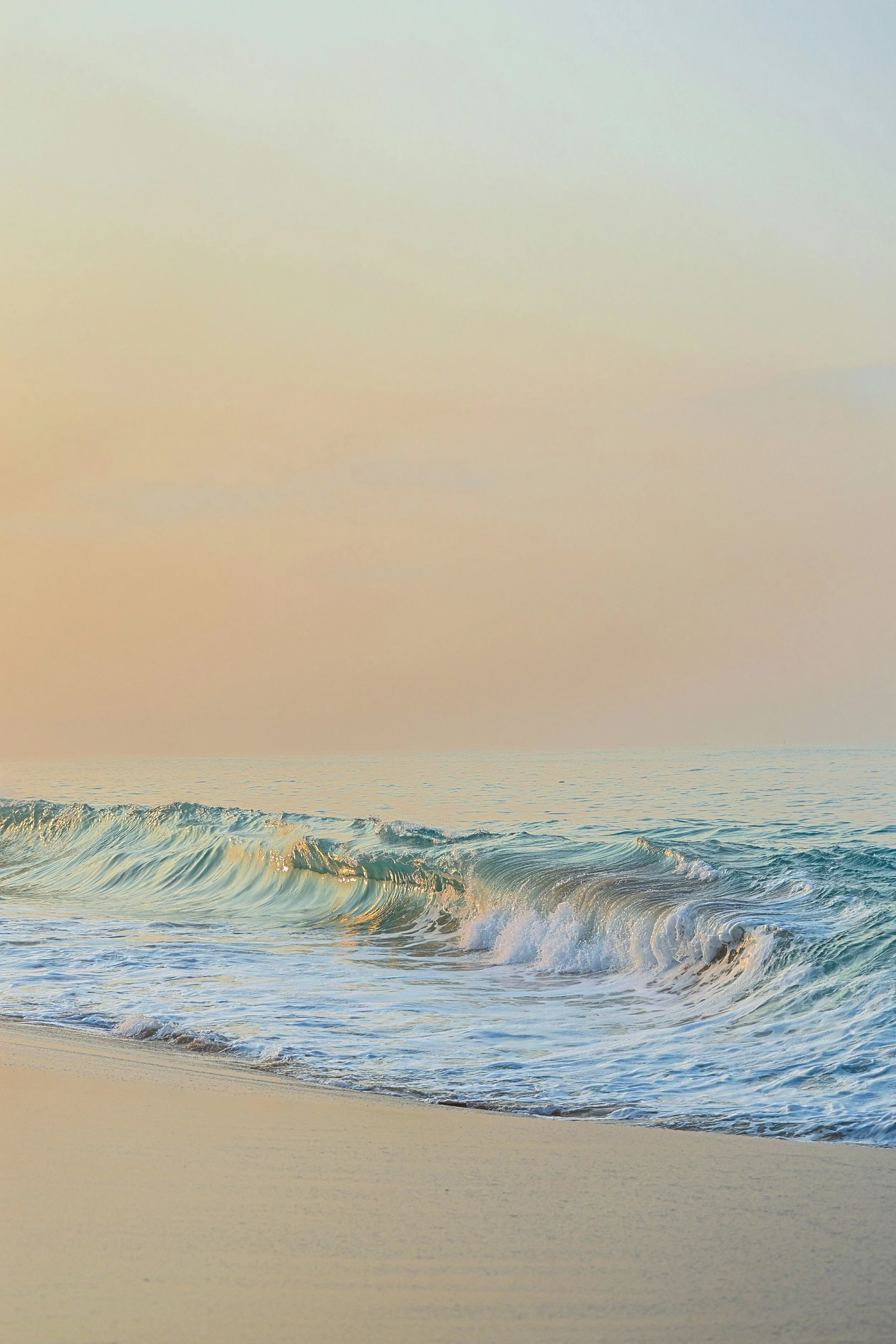 A beach scene with waves crashing onto the sandy shore during the daytime.