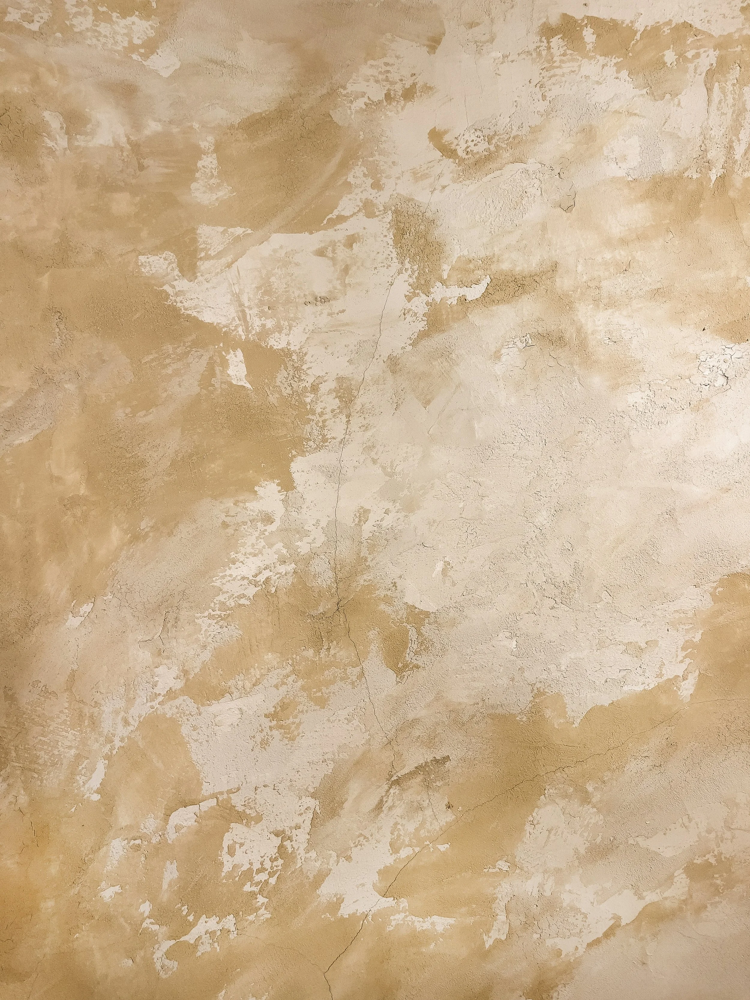 Close-up of a beige plaster wall with peeling and cracked paint, showing areas of exposed surface and distressed texture.
