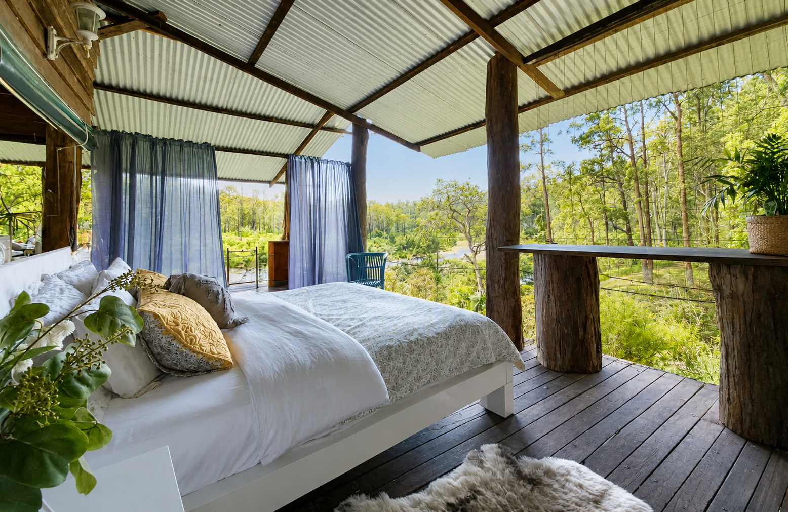 A cozy bedroom with an expansive view of lush green trees, a white bed with various pillows, purple curtains, a wooden floor, and rustic wooden counters.