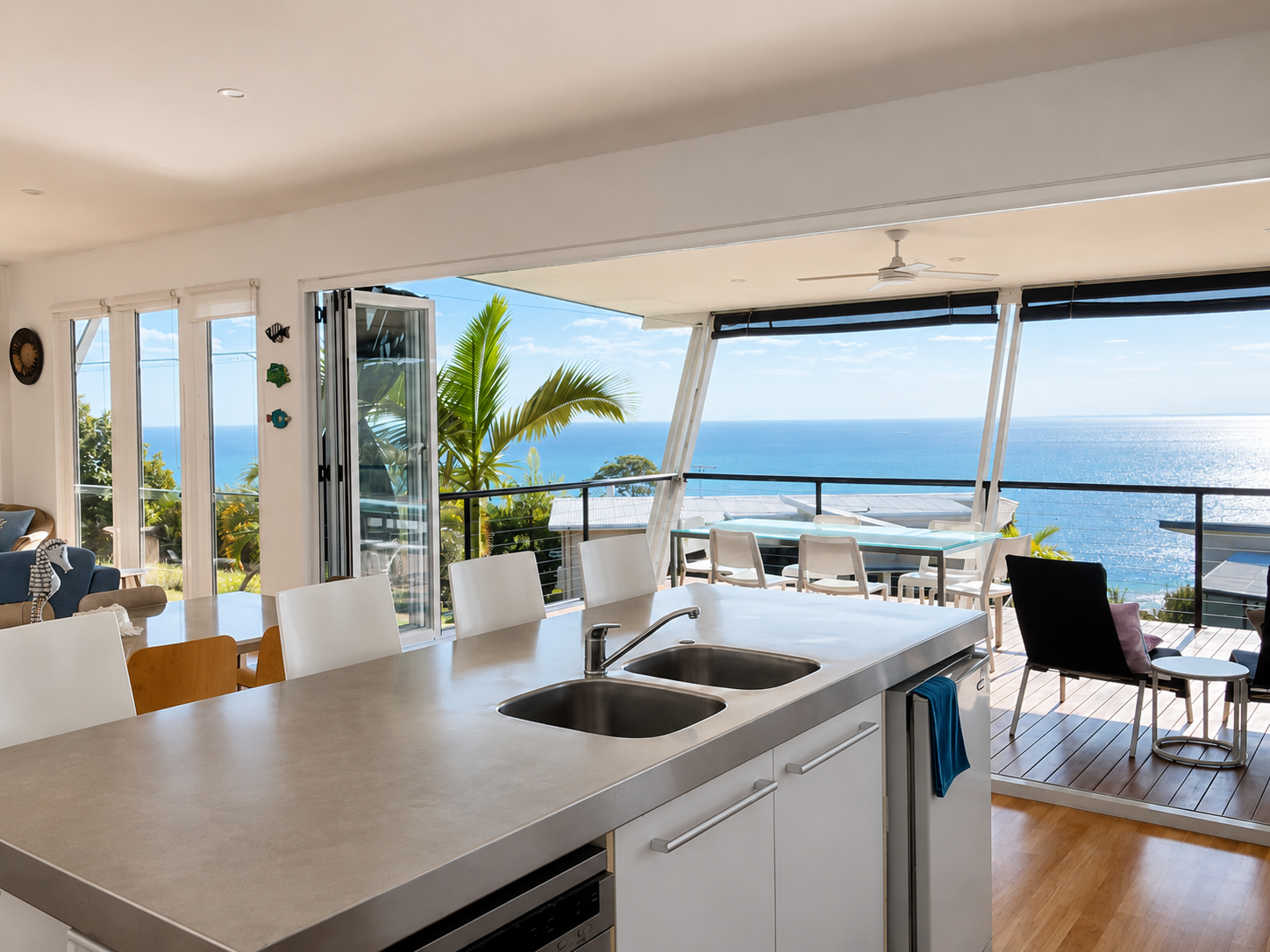 Open kitchen with view of ocean, balcony with chairs, dining table, palm tree outside, and sliding glass doors