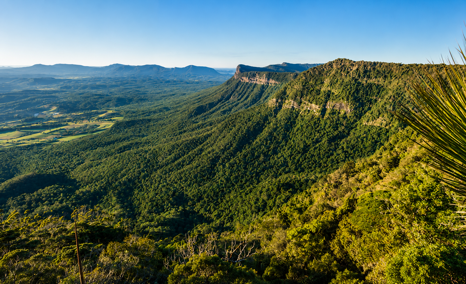 A scenic view of lush green mountains and valley, with a clear blue sky overhead.