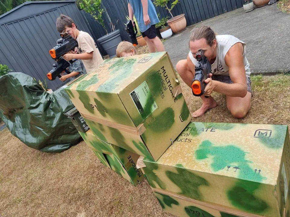 Kids creating a DIY backyard laser tag arena with cardboard forts and cover during a home birthday party