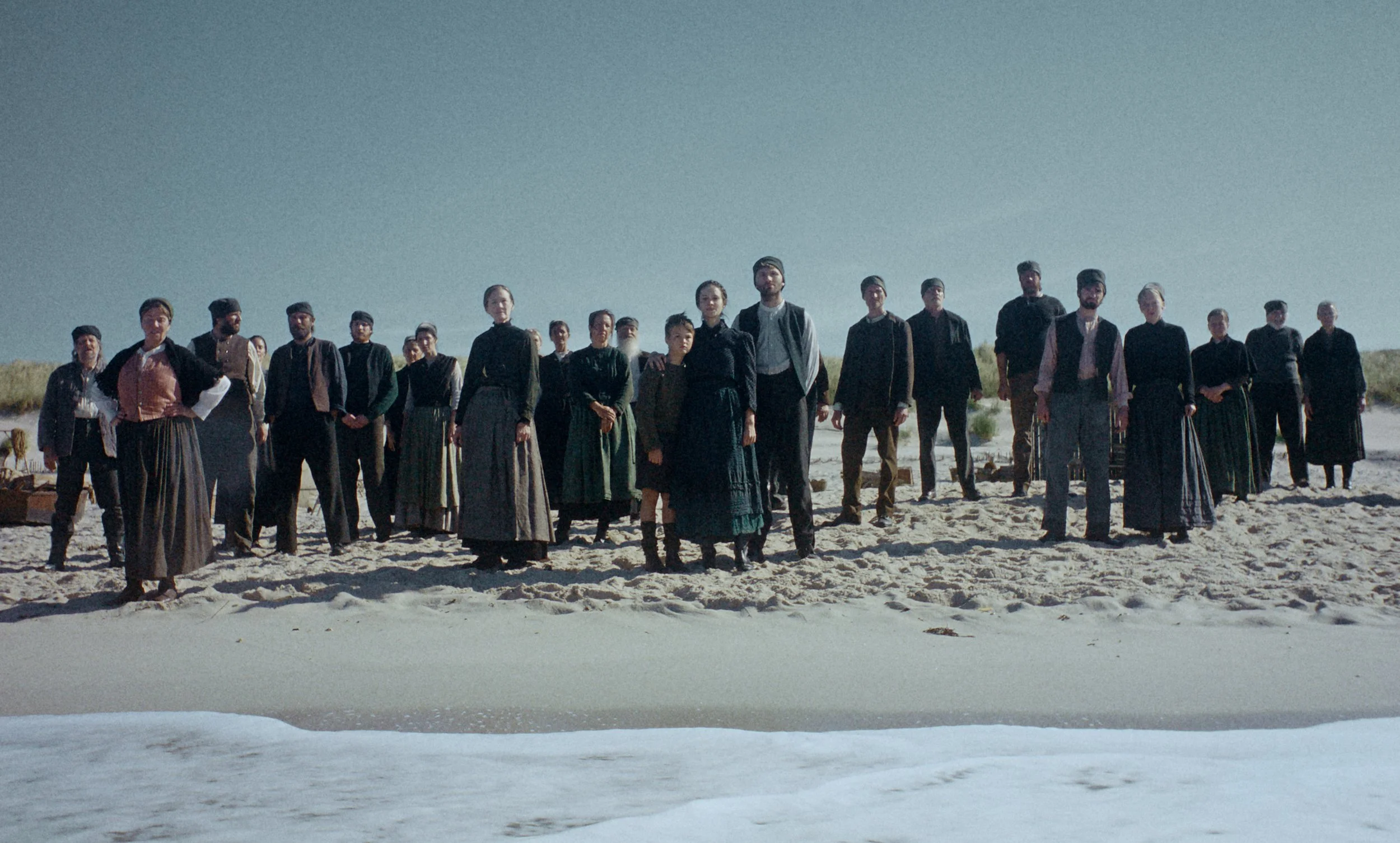 A group of people dressed in historical clothing standing on a sandy beach under a clear sky.