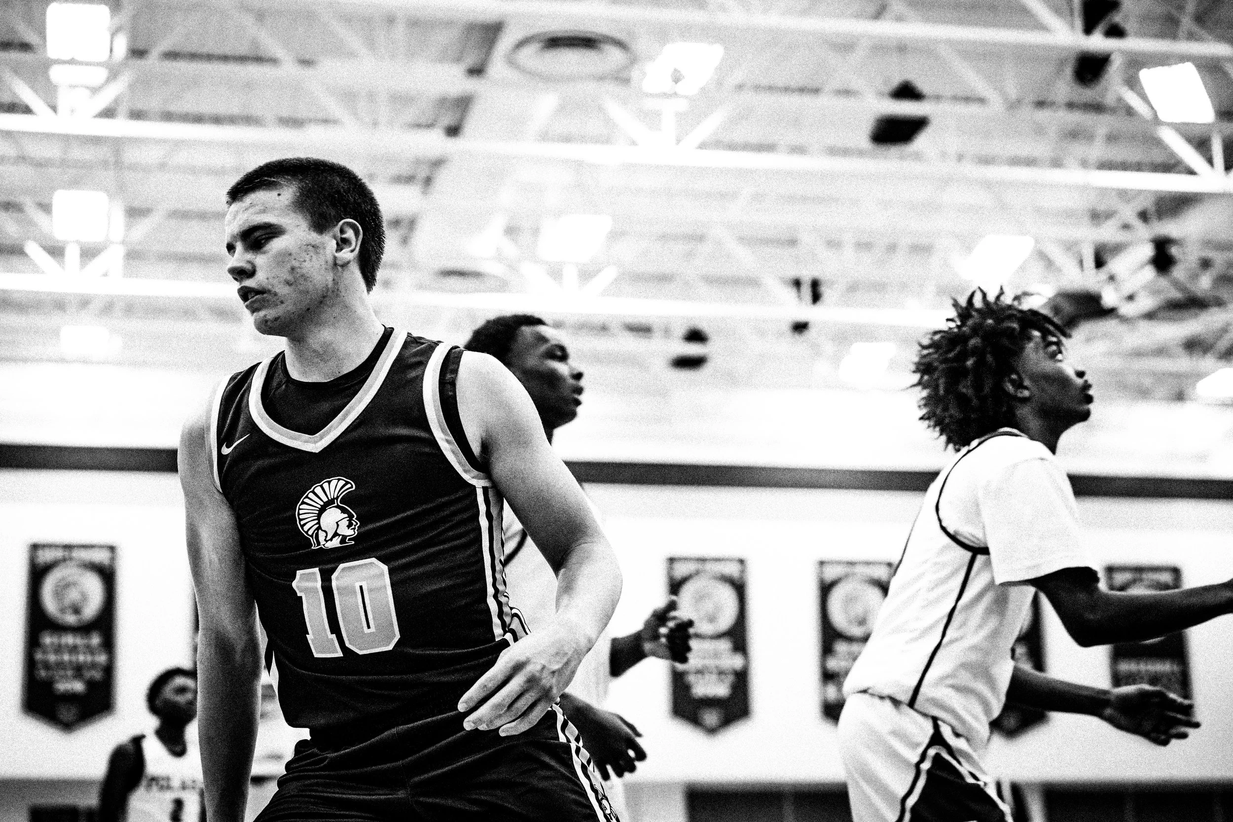Black and white photo of basketball players warming up in a gym, with a young man with short hair and a jersey number 10 at the forefront.