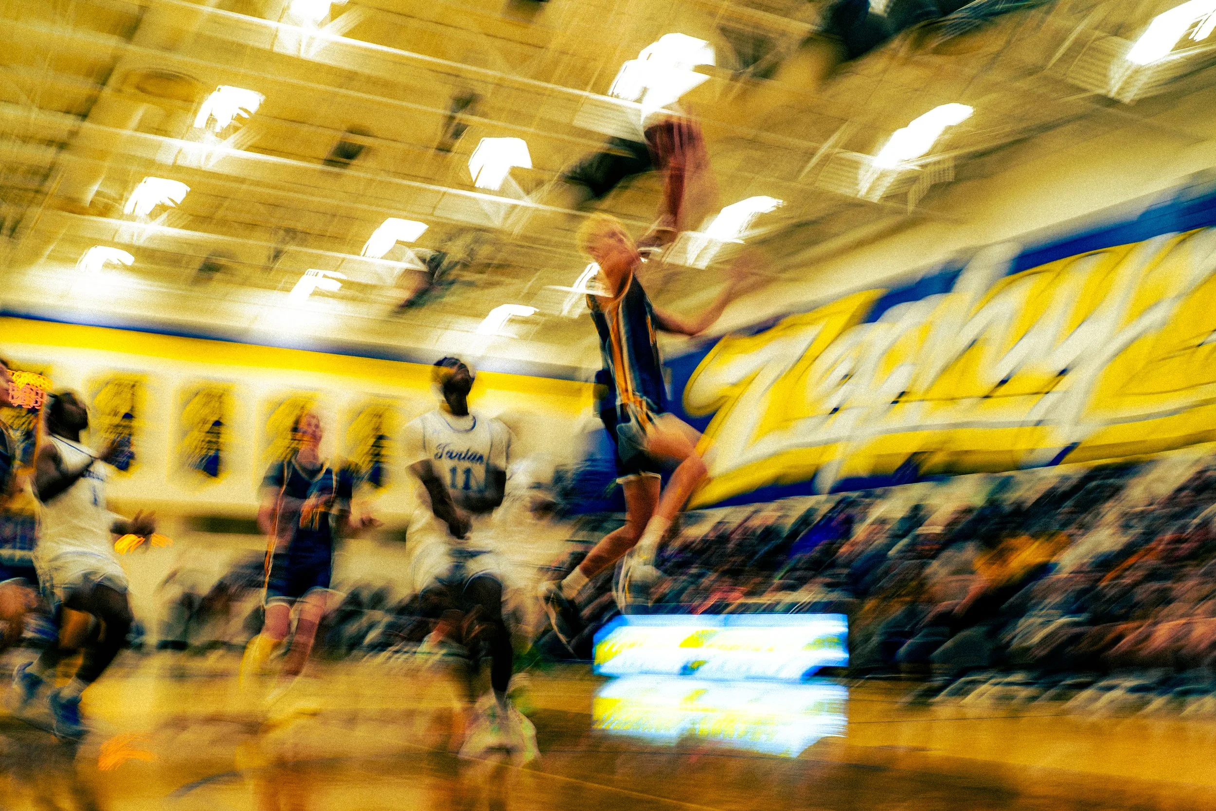 Blurred image of a volleyball game with players jumping to hit the ball inside a gymnasium.