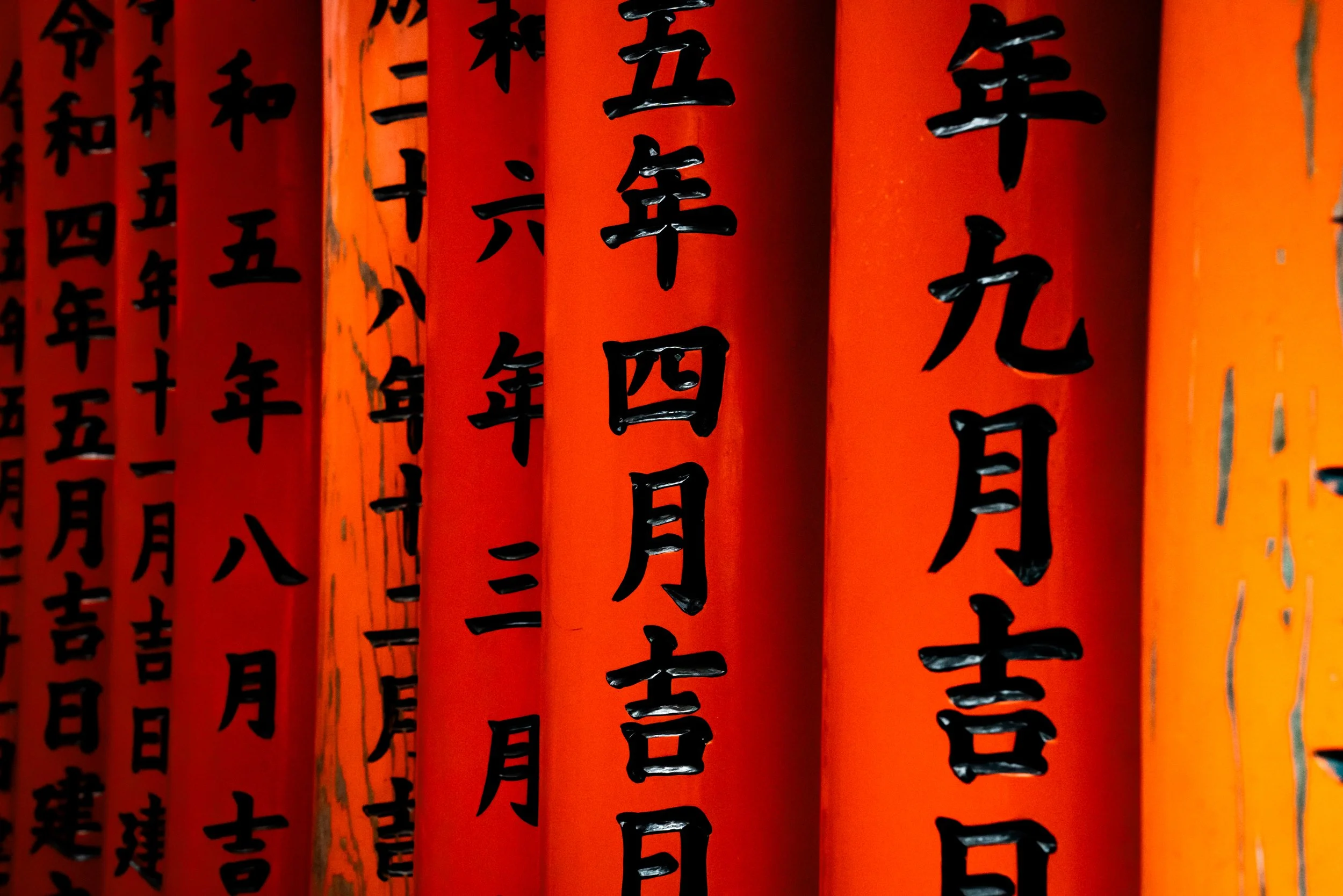 Close-up of orange paper or fabric strips with black Chinese or Japanese calligraphy characters written vertically in rows.