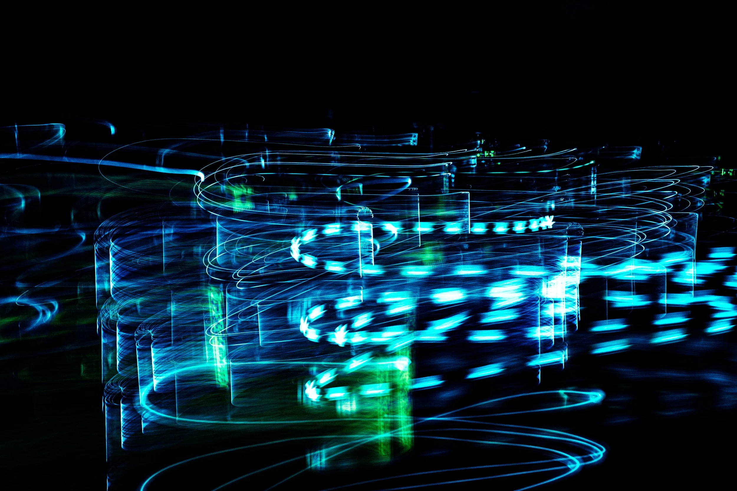 Long exposure photo of colorful blue and green light trails on a dark background.