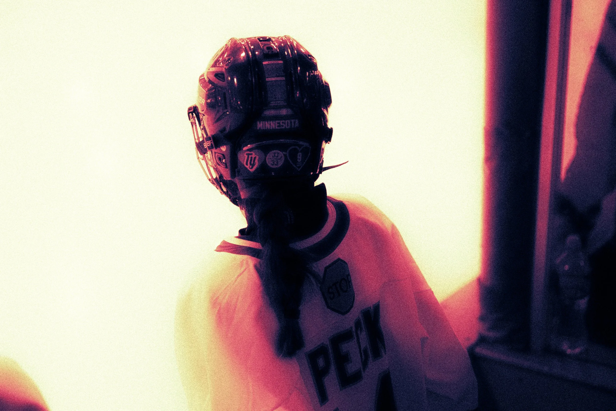 A hockey player wearing a Minnesota jersey and a helmet, seen from the side in a dimly lit setting.