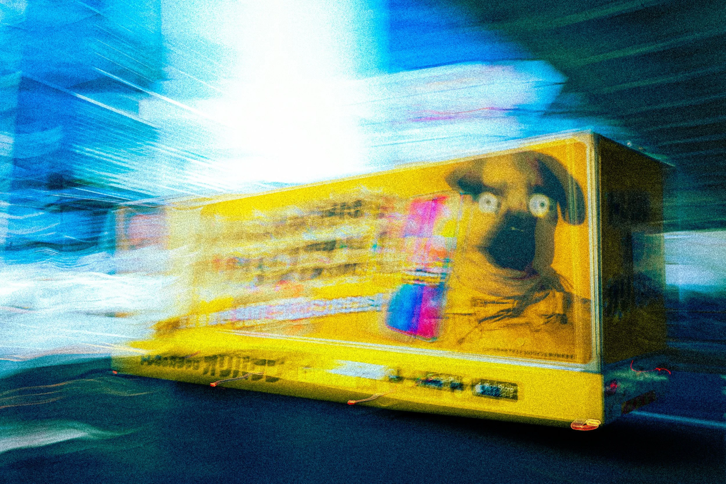 A blurry, colorful image of a yellow toy truck with a character face on the side, set against a background of bright, streaked lights.